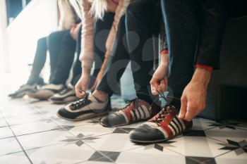 Bowling alley players ties shoelaces on house shoes. Bowlers sitting on the bench and prepares to competition in club, active sport. Bowl sport