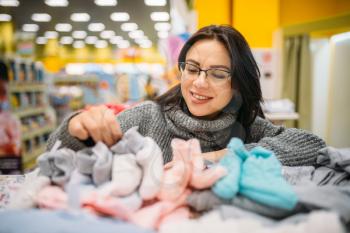 Cheerful future mother in glasses buys baby clothes in the store for newborns. Pregnant woman in shop of goods for infants