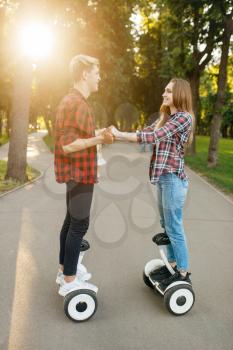 Young couple riding on gyro board in park. Outdoor recreation with electric gyroboard. Transport with balance technology
