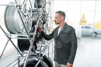 Man choosing wheels for new car in showroom. Male customer buying vehicle in dealership, automobile sale, auto purchase