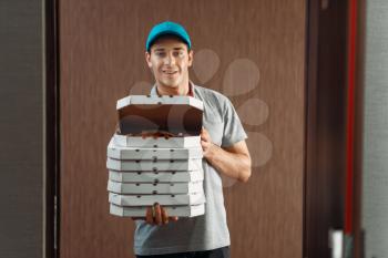 Delivery man shows fresh pizza in box, delivering service. Courier from pizzeria holds cardboard packages indoors