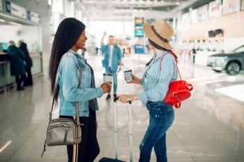 Two female tourists with cases meet a friend in airport. Passengers with baggage in air terminal, happy journey, summer travel