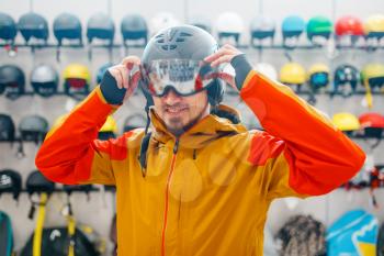 Man at the showcase trying on helmet for ski or snowboarding, side view, sports shop. Winter season extreme lifestyle, active leisure store, buyers choosing protect equipment