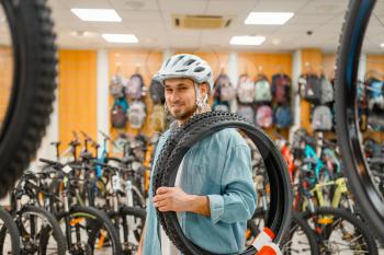 Man in cycling helmet holds bicycle tyres, shopping in sports shop. Summer season extreme lifestyle, active leisure store, customers buying bike equipment