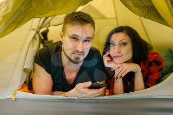 Couple with phone lying in tourist tent, customers in sports shop. Active leisure, professional travelling equipment