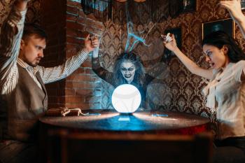 Female foreteller calls the spirits, witchcraft. Scary witch reads a magic spell over a crystal ball, young people hands up on spiritual seance