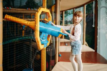 Funny girl plays with air gun in children game center. Excited child having fun on playground indoors. Female kid playing in amusement centre