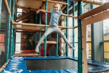 Funny girl jumping on the trampoline, children game center. Excited child having fun on playground indoors. Female kid playing in amusement centre