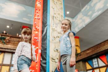 Two little girls looks on climbing wall, children game center. Excited childs having fun on playground indoors. Kids playing in amusement centre