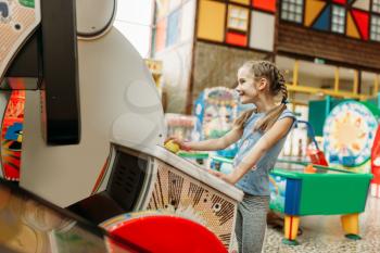 Little girl plays on video game machine, children entertainment center. Excited childs having fun on playground indoors. Kids playing on motorcycles, amusement centre