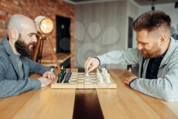 Male chess players begin playing, the first move. Two chessplayers begin the intellectual tournament indoors. Chessboard on wooden table, strategy game