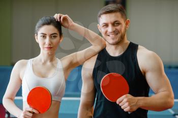 Man and woman holds ping pong rackets indoors. Couple in sportswear plays table tennis in gym. Male and female persons in table-tennis club