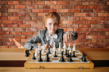 Clever schoolgirl, chess player at the table. Young girl at the chessboard, female kid plays logic game