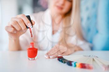 Beautician salon, manicure, woman with red nail varnish. Hands care treatment for female client in beauty shop, customer at the cosmetologist, master works with fingernails