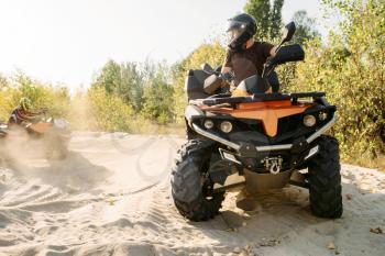 Two atv riders in helmets ride in a circle on sand, offroad in forest. Riding on quad bike, extreme sport and travelling, quadbike summer adventure