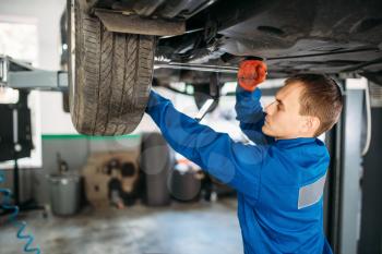 Mechanic with a wrench repairs the suspension, car on the lift. Tire service, vehicle maintenance