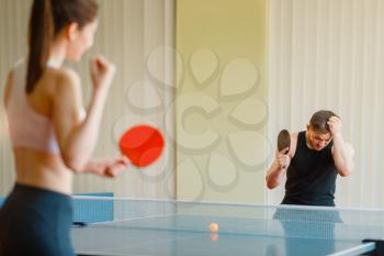Man and woman playing ping pong indoors, girl winner. Couple in sportswear holds rackets and plays table tennis in gym