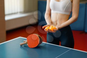 Young woman holds ping pong balls at the game table indoors. Female person in sportswear, training in table-tennis club