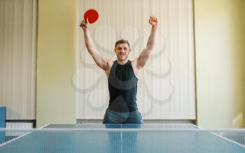 Happy man with ping pong racket raised his hands up, tournament indoors. Male person in sportswear, training in table tennis club