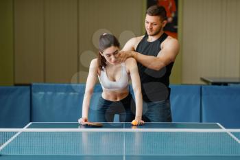 Man doing massage to woman, ping pong training indoors. Couple in sportswear holds rackets and plays table tennis in gym