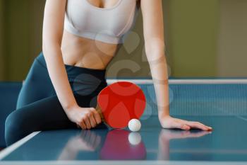Woman with racket and ball poses at the ping pong table indoors. Female person in sportswear, training in table tennis-club