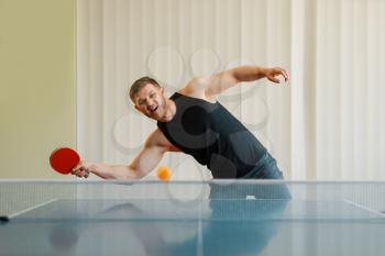 Man with ping pong racket plays the ball off, image in action, workout indoors. Male person in sportswear, training in table tennis club