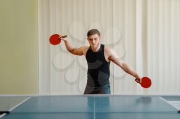 Man with two rackets playing ping pong indoors. Male person in sportswear, training in table tennis club