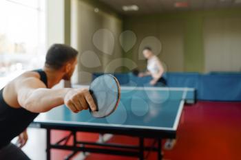 Man and woman playing ping pong indoors, focus on racket. Couple in sportswear plays table tennis in gym. Male and female persons in table-tennis club