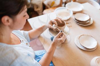 Female potter skins pot with a spatula, pottery workshop. Woman molding a bowl. Handmade ceramic art, tableware from clay