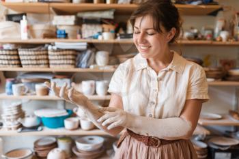 Female master hands covered with dried clay, pottery workshop interior on background. Woman molding a bowl. Handmade ceramic art, tableware making