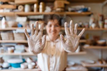 Female potter shows hands covered with dried clay, pottery workshop interior on background. Woman molding a bowl. Handmade ceramic art, tableware making