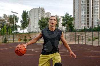 Basketball player with ball in motion on outdoor court. Male athlete in sportswear shoots on streetball training, jump in action
