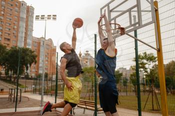 Two basketball players playing on outdoor court. Male athletes in sportswear play the game on streetball training
