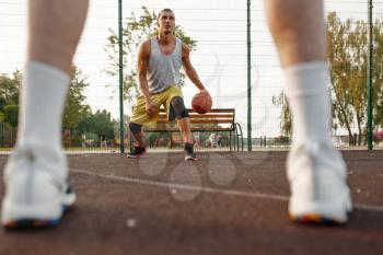 Male basketball player with ball shows his skill on outdoor court. Male athlete in sportswear on streetball training, summer stadium