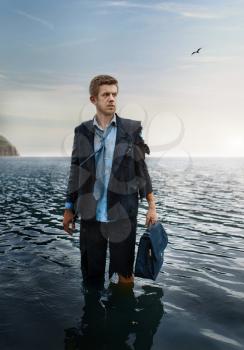 Alone businessman with briefcase standing in the sea, desert island. Business risk, collapse or bankruptcy concept