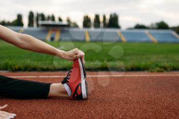 Female runner in sportswear, workout on stadium. Woman doing stretching exercise before running on outdoor arena