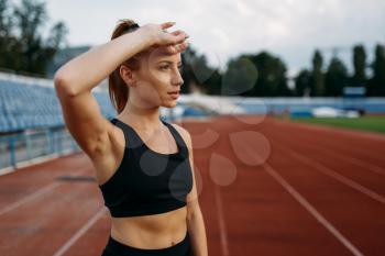 Tired female runner in sportswear, training on stadium. Woman doing stretching exercise before running on outdoor arena