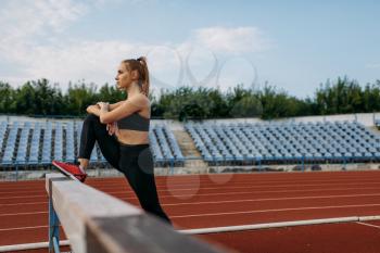 Female runner in sportswear, stretching workout on stadium. Slim woman doing exercise before running on outdoor arena