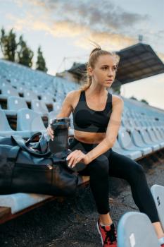 Female jogger in sportswear sitting on tribune, training on stadium. Woman doing stretching exercise before running on outdoor arena