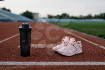 Sport shoes and bottle of water on stadium, nobody. Running or fitness training concept, healthy lifestyle