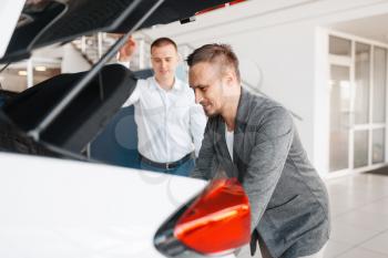 Buyer and manager looks at the trunk of new car in showroom. Male customer choosing vehicle in dealership, automobile sale, auto purchase