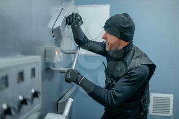 Bank robbery, male robber in black uniform trying to open vault lock. Criminal profession, theft concept