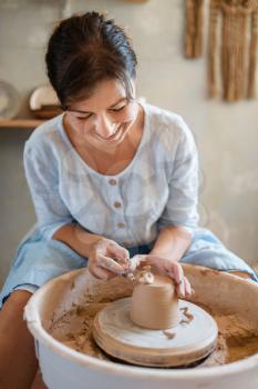 Female potter removes the extra layer on pot, pottery wheel. Woman molding a bowl. Handmade ceramic art, tableware from clay