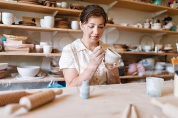 Female master paints a pot, pottery workshop. Woman molding a bowl. Handmade ceramic art, tableware from clay