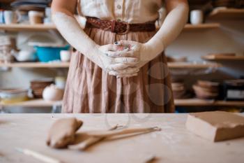 Female artisan hands covered with dried clay, pottery workshop interior on background. Woman molding a bowl. Handmade ceramic art, tableware making