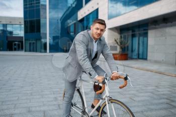 Young businessman in suit on the bicycle in downtown. Business person on eco transport on city street