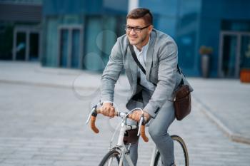 One businessman poses on bicycle at the office building in downtown. Business person riding on eco transport on city street