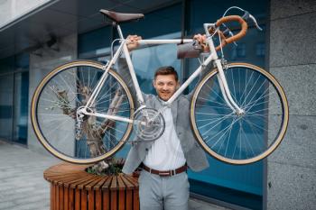 Strong businessman holds bicycle at the glass office building in downtown. Business person riding on eco transport on city street, urban style