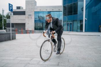 One businessman in funny glasses poses on bicycle at the office building in downtown. Business person riding on eco transport on city street
