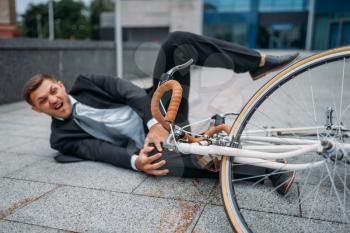Businessman fell off his bike at the office building in downtown. Business person riding on eco transport on city street